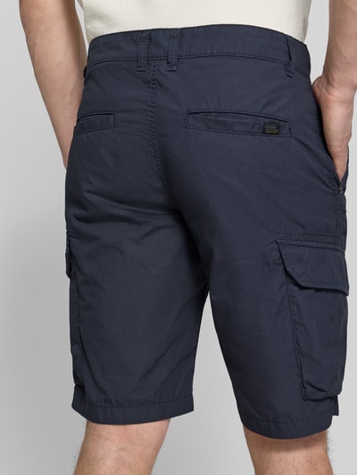 Mężczyzna nosi Bermudas mit Cargotaschen von camel active w kolorze granatowym, czysta bawełna, krój regular fit, kieszenie boczne i cargo, detal z logo, szerokość w rozmiarze 32: 44 cm, długość wewnętrzna nogawki w rozmiarze 32: 26 cm, całkowity widok z tyłu.
