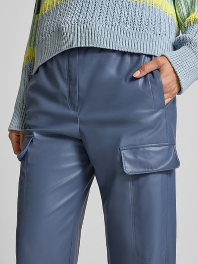 Frauenmodel trägt Straight Fit Hose in Leder-Optik mit Pattentaschen von Marc Cain, elastischer Bund, glatte Oberfläche, Nahaufnahme Oberkörper.
