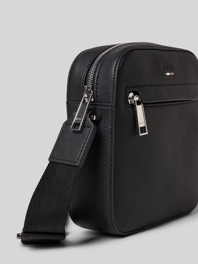 Produktfoto, Crossbody Bag mit Label-Detail Modell 'Ray' von BOSS, czarny materiał z fakturowanym wzorem, główna przegroda na zamek błyskawiczny, regulowany pasek na ramię, przegródka zapinana na zamek błyskawiczny z przodu, szerokość 17 cm, długość 19 cm, głębokość 6 cm, długość paska na ramię 120 cm.