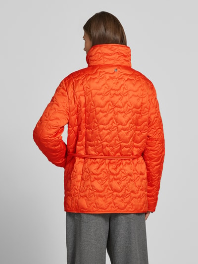 Vrouwenmodel draagt feloranje gewatteerd jack met opgestikte zakken en strikceintuur van Marc Cain, regular fit, opstaande kraag, knoopsluiting, ruglengte maat M 70 cm, schouderbreedte 45 cm, borstwijdte 43 cm, mouwlengte 62 cm, volledig van achteren.