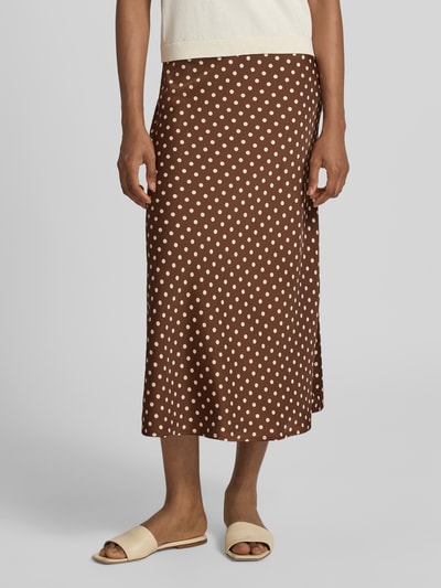 Kobiece model prezentuje spódnica midi w brązowym kolorze z beżowym wzorem na całej powierzchni, Linia a, Mieszanka materiałów z dodatkiem streczu, Model 'PELLA' od YAS, Szerokość w rozmiarze S: 36 cm, całkowita długość w rozmiarze S: 84 cm, widok całej sylwetki z przodu.