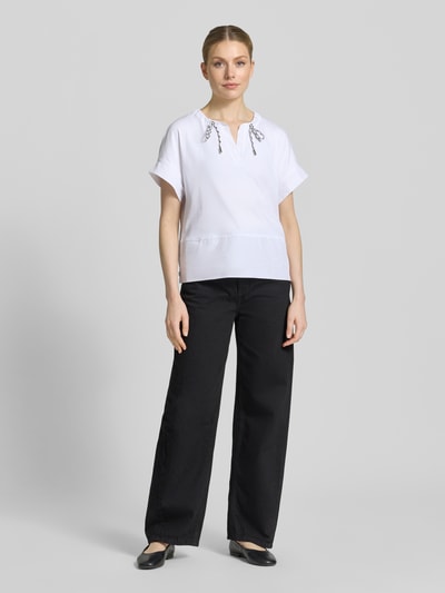 Modelka kobieca nosi T-Shirt mit Tunikakragen und Kordelzug od Marc Cain, biały bawełniany mix z elastanem, prosty krój, detal z logo, długość tyłu 55 cm dla rozmiaru 36, pełny widok od przodu.