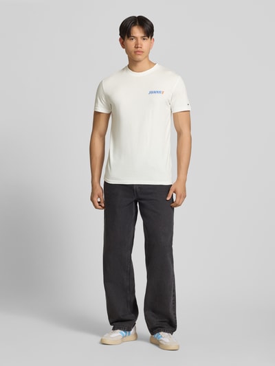 Männermodel trägt Regular Fit T-Shirt aus reiner Baumwolle von Tommy Jeans, unifarben, Rundhals, kurzarm, Label Print, Ganzkörperansicht von vorne.