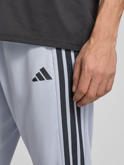 Männermodel trägt Slim Fit Sweatpants mit Logo-Print von adidas Training, helle Farbe, Logo-Print, Slim-Fit, Reißverschluss-Eingrifftaschen, Elastischer Bund, Detailaufnahme Hüfte