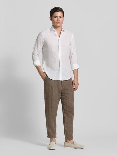 Męski model nosi Relaxed Fit Stoffhose aus Leinen-Baumwoll-Mix Modell 'RON' od SELECTED HOMME, melanżowy brąz, tkanina twill, spodnie z zakładkami, niska talia, długość cropped, przód z guzikami i ukrytym zamkiem, wpuszczane kieszenie, tylne kieszenie z guzikiem, widok całej sylwetki z przodu.