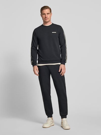 Männermodel trägt schwarze Sweatpants aus Baumwoll-Mix von EA7 Emporio Armani mit Tunnelzug, elastischem Bund und Eingrifftaschen, Ganzkörperansicht von vorne.