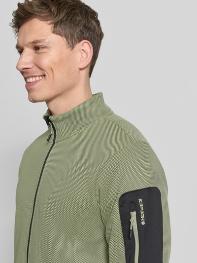 Męski model nosi Regular Fit Fleecejacke mit Stehkragen Modell 'BREDSTEDT' od Icepeak, jasnozielony materiał, czarna kieszeń na rękawie, krój regular fit, kieszenie i mankiety elastyczne, zamek, kontekst: długość pleców 69 cm, szerokość ramion 43 cm, szerokość w rozmiarze M: 54 cm, długość rękawa 67 cm, zbliżenie na górną część ciała, widok z przodu.