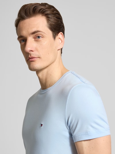 Mannenmodel draagt 'Slim Fit T-Shirt aus Baumwoll-Mix' van Tommy Hilfiger in lichtblauw, unicolor, slim fit, logodetail, ronde hals, korte mouw, stretch katoenmix. Nahaufnahme bovenlichaam.