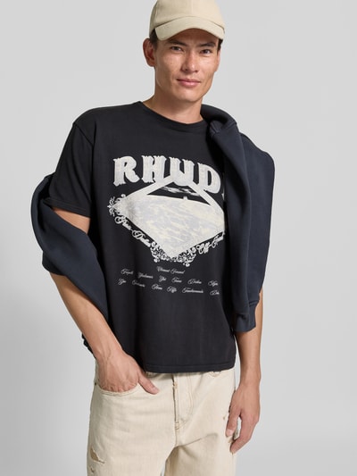Männermodel trägt T-Shirt mit großem Frontprint von RHUDE in Schwarz, Motiv-Print, Regular Fit, Longline, Rundhals, Baumwolle, Ganzkörperansicht von vorne.