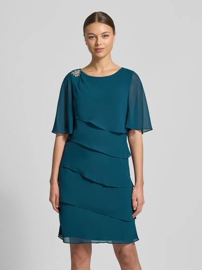 Frauenmodel trägt Relaxed Fit Kleid mit Ziersteinbesatz von Christian Berg Cocktail in Petrol, halbarm, rundhals, semitransparent, Ganzkörperansicht von vorne
