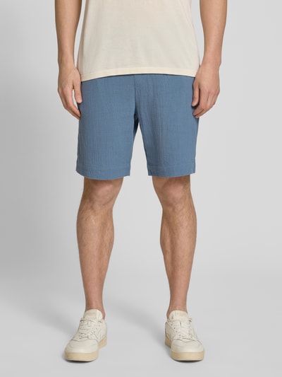 Männermodel trägt Regular Fit Shorts aus reiner Baumwolle Modell 'REGCAL' von SELECTED HOMME, Optik: Unifarben, Eingrifftaschen, Bundabschluss elastisch mit Tunnelzug, Gesäßtasche, Farbe Blau, Struktur leicht texturiert, Ganzkörperansicht von vorne.