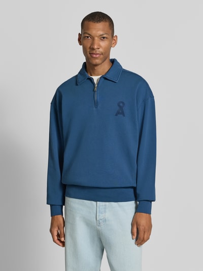 Männermodel trägt Relaxed Fit Troyer aus reiner Baumwolle Modell 'ICONIC Å GMT' von ARMEDANGELS, Blau, glatte Textur, Ganzkörperansicht von vorne.