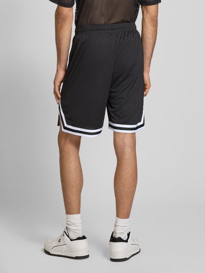 Männermodel trägt Relaxed Fit Shorts mit Logo-Stitching von KARL KANI in Schwarz mit Mesh-Design, Elastikbund, Ganzkörperansicht Rückansicht.