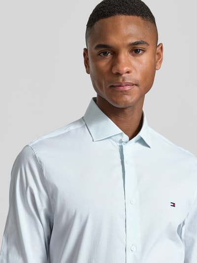 Männermodel trägt Slim Fit Businesshemd aus bawełny-mix von Tommy Hilfiger, efekt: wzór w paski, wyhaftowane logo, krój slim fit, kołnierzyk typu kent, listwa guzikowa na całej długości, mankiet zapinany na 1 guzik, mieszanka bawełny, kolor jasnoniebieski, nahaufnahme górna część ciała