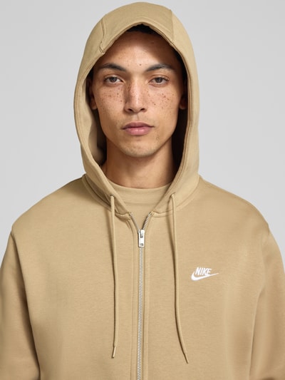 Männermodel trägt Regular Fit Sweatjacke aus Baumwoll-Mix von Nike in Beige mit Reißverschluss und Logostick, Nahaufnahme Oberkörper.