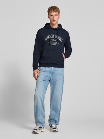 Männermodel trägt Regular Fit Hoodie aus Baumwoll-Mix Modell 'Denver' von JACK & JONES, dunkelblau, Känguru-Tasche, Ganzkörperansicht von vorne.