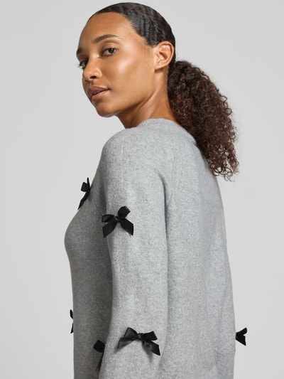 Frauenmodel trägt Regular Fit Pullover mit Raglanärmeln Modell 'NOELLE' von ONLY, hellgrau mit schwarzen Schleifen, Nahaufnahme Oberkörper, Damen Pullover von ONLY.