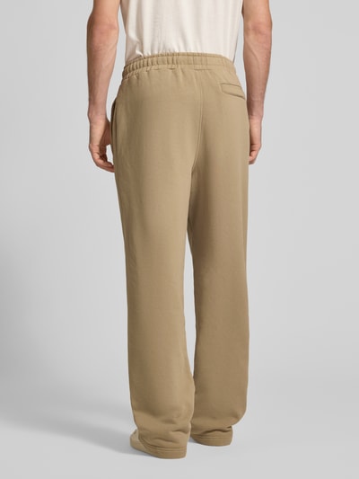 Männermodel trägt Loose Fit Sweatpants aus Baumwoll-Mix mit Label-Detail von PEGADOR in beige, elastischer Bund, Ganzkörperansicht Rückansicht.