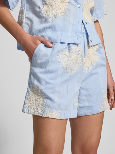 Frauenmodel trägt Straight Fit Shorts mit floralen Zierapplikationen Modell 'Kana' von YAS aus Reine Baumwolle, Nahaufnahme Oberkörper.
