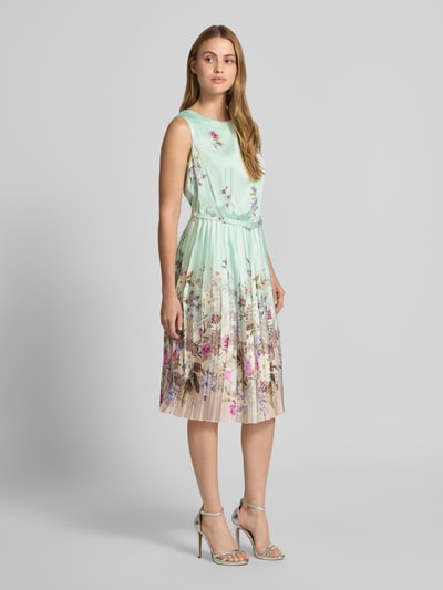 Frauenmodel trägt Knielanges Cocktailkleid mit Plisseefalten von Rinascimento in Mint mit floralen Mustern, A-Linie, Ganzkörperansicht von vorne.