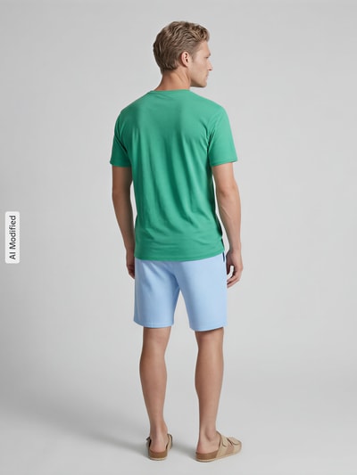 Männermodel trägt Regular Fit T-Shirt mit V-Ausschnitt von MCNEAL in Grün aus reiner Baumwolle, Rollsaum, Ganzkörperansicht Rückansicht.