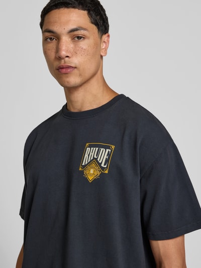 Männermodel trägt T-Shirt mit Label-Print von RHUDE in Schwarz, Reine Baumwolle, Gerader-Schnitt, Rundhalsausschnitt, Kurzärmelig, Nahaufnahme Oberkörper.