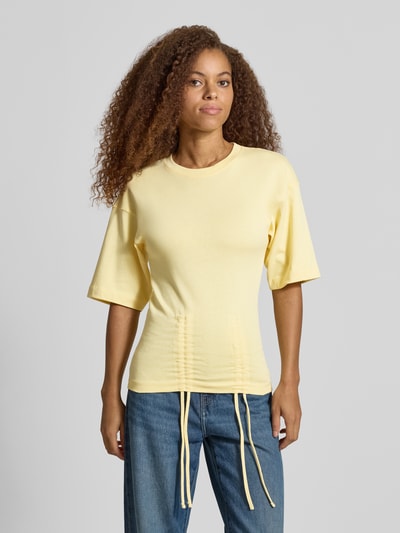 Kobiece model prezentuje damski t-shirt z bawełny o prostym kroju, model 'MALLE' od Topshop, okrągły dekolt, marszczenia z wiązaniem, opuszczone ramiona, długość tyłu w rozmiarze S: 66 cm, widok całej sylwetki z przodu.