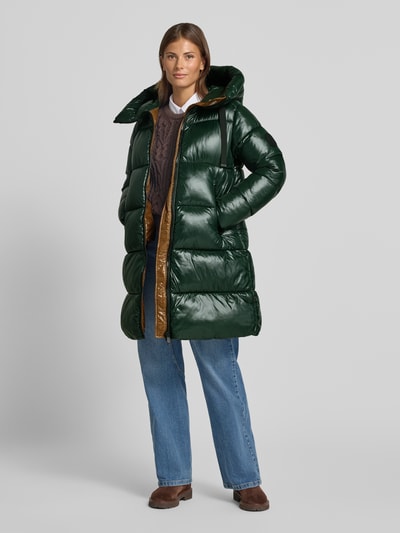 Frauenmodel trägt dunkelgrünen, glänzenden Steppmantel mit Kapuze und Label-Patch Modell 'ISABEL' von Save The Duck, Ganzkörperansicht von vorne. Gerader Schnitt, Zweiwege-Reißverschluss, seitliche Reißverschlusstaschen, Maße entsprechen Größe S.