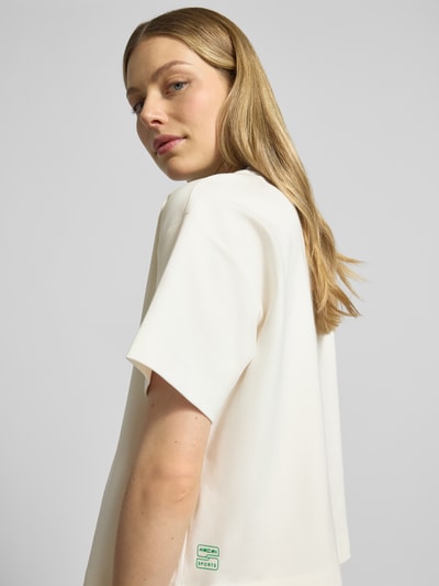 Frauenmodel trägt Relaxed Fit T-Shirt mit Motiv-Applikation von Marc Cain aus elastischem Baumwoll-Modal-Mix, Rundhalsausschnitt, Nahaufnahme Oberkörper.