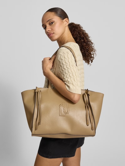 Frauenmodel trägt Tote Bag mit Logo-Detail Modell 'Lapis' von Liu Jo White in Beige mit Leder-Optik, Hauptfach, schmale Schulterriemen, Reißverschlussfach innen, Ganzkörperansicht von vorne.