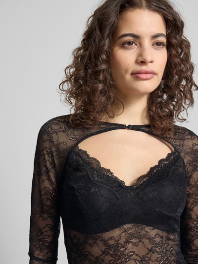Frauenmodel trägt Longsleeve mit Cut Out von Gina Tricot in Schwarz, semitransparentem Spitzenmaterial, körpernah, Knopfverschluss, Nahaufnahme Oberkörper.