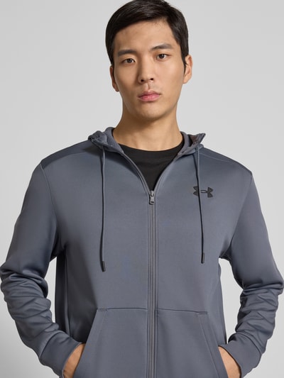 Männermodel trägt Sweatjacke mit Kapuze von Under Armour in Grau mit Lockerer-Schnitt, Tunnelzug, Reißverschluss, Label-Detail, Eingrifftaschen, Gerippte-Abschlüsse, Nahaufnahme Oberkörper.