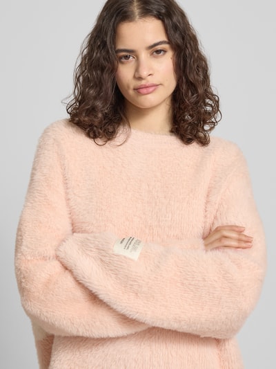 Frauenmodel trägt Oversized Strickpullover mit Label-Detail von Karo Kauer in Pastellrosa, weiche Textur, Nahaufnahme Oberkörper.