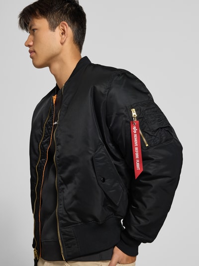 Männermodel trägt Bomberjacke mit Pattentaschen und Label-Applikation von Alpha Industries in Schwarz, Reißverschluss, Nahaufnahme Oberkörper. Rückenlänge 69 cm, Schulterbreite 44 cm, Brustweite 54 cm, Ärmellänge 64 cm, Regular Fit.