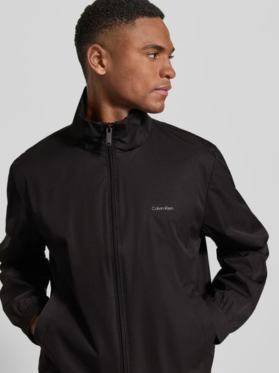 Männermodel trägt Jacke mit Stehkragen und Logo von Calvin Klein in Schwarz, Regular Fit, Reißverschluss, Eingrifftaschen, Nahaufnahme Oberkörper.