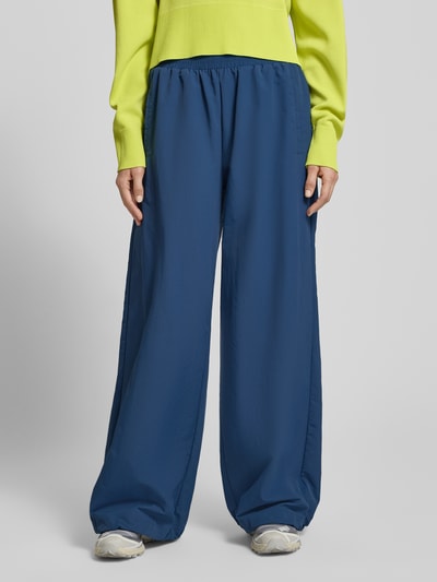 Frauenmodel trägt Nylon-Ballonhose im 90s-Stil - curated by Tinvcb von Tinvcb, relaxed Fit, Elastikbund, Eingrifftaschen, blaue Farbe, glatte Textur, Ganzkörperansicht von vorne.