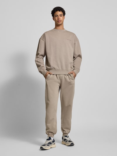 Männermodel trägt Oversized Sweatshirt mit Label-Stitching von Pegador in Beige, Baumwoll-Mix, Gerippte-Abschlüsse, Rundhalsausschnitt, oversized, Rückenlänge 71 cm, Ärmellänge 68 cm, Ganzkörperansicht von vorne.
