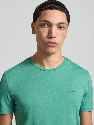 Männermodel trägt Slim Fit T-Shirt aus Baumwoll-Mix Modell 'JASPE HERITAGE' von Tommy Jeans in Melange-Optik, Logo-Stitching, Nahaufnahme Oberkörper.