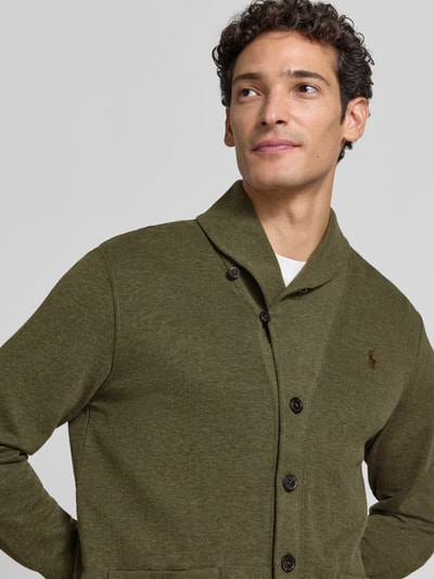 Männermodel trägt Regular Fit Strickjacke aus Baumwoll-Mix von Polo Ralph Lauren in Olivgrün mit sichtbarer Knopfleiste, Nahaufnahme Oberkörper. Herren Strickjacke von Polo Ralph Lauren.