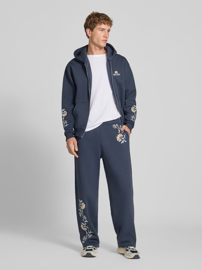 Männermodel trägt Straight Fit Sweatpants mit floraler Stickerei von REVIEW in Dunkelblau, Baumwoll-Mix, Ganzkörperansicht von vorne.