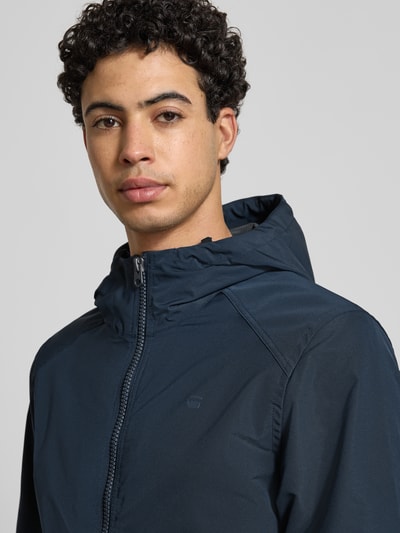 Mannelijk model draagt Regular fit jack met logoprint model 'Track' van G-Star Raw in donkerblauw, Nahaufnahme Oberkörper, Heren jack, capuchon met opstaande kraag, steekzakken, elastische boorden, ruglengte maat M 65 cm, schouderbreedte 41 cm, borstwijdte 48 cm, mouwlengte 67 cm.