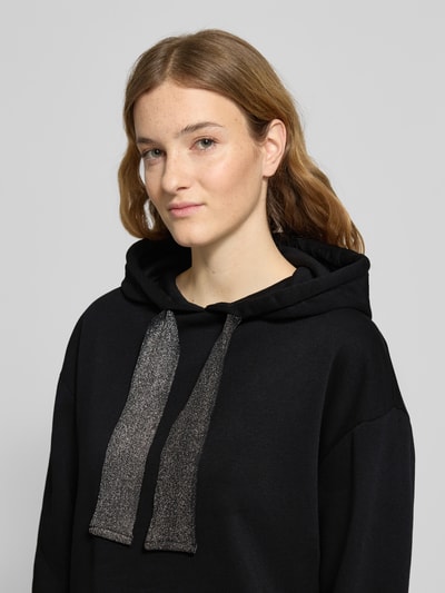 Modelka kobieca ma na sobie Regular Fit Hoodie aus Baumwoll-Mix Modell 'CHILLI' od Pieces, czarny, gładki, z kapturem i długimi rękawami, z label stitching, materiał sweat, krój regular fit, widok z przodu, zbliżenie na górną część ciała.