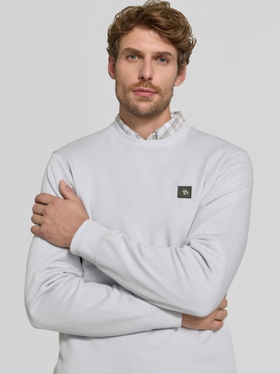 Männermodel trägt Sweatshirt mit Label-Patch von Scotch & Soda aus bawełna, luźny krój, okrągły dekolt, prążkowane wykończenia, Długość tyłu w rozmiarze M: 64 cm, Długość rękawów w rozmiarze M: 64 cm, jasnoszary kolor, gładka faktura, Nahaufnahme Oberkörper