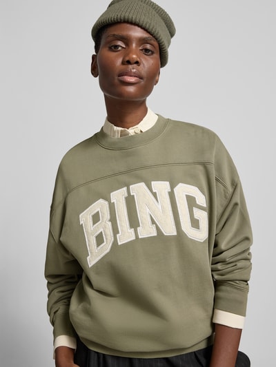 Frauenmodel trägt Oversized Sweatshirt aus Baumwolle von Anine Bing in Olive mit Rundhalsausschnitt, Label-Detail und elastische Abschlüsse, Rückenlänge bei Größe S 61 cm, Nahaufnahme Oberkörper.
