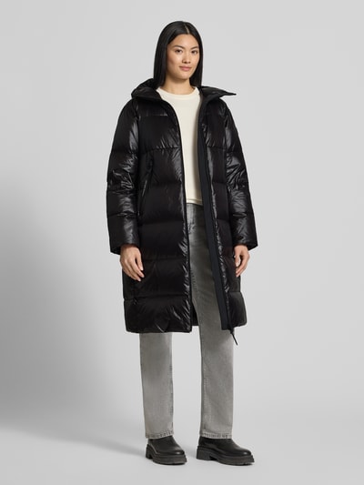 Frauenmodel trägt Mantel mit Kapuze Modell 'SELECTRIC' von Peuterey in Schwarz mit Steppnähten, Zweiwege-Reißverschluss und Reißverschlusstaschen, gerade Passform, Label-Detail, Ganzkörperansicht von vorne.