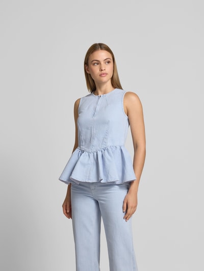Frauenmodel trägt Slim Fit Top in Denim-Optik von BAUM & PFERDGARTEN in Hellblau mit Rüschenbesatz und Reißverschluss, Nahaufnahme Oberkörper.