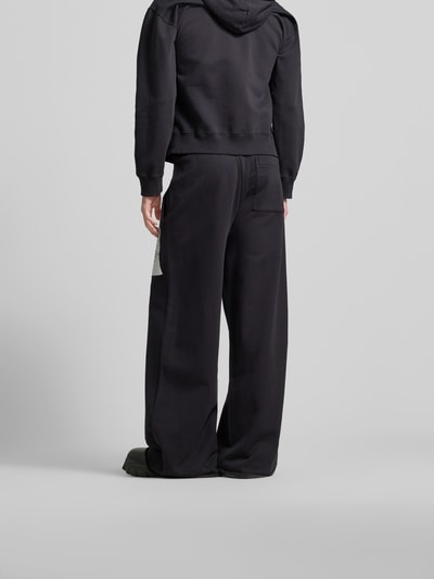 Männermodel trägt Loose Fit Stoffhose mit Logo-Print von MM6 Maison Margiela in Schwarz, Baumwolle, Rückansicht, Ganzkörperansicht