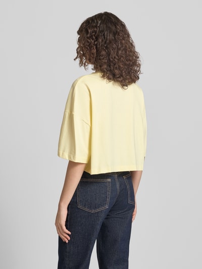 Frauenmodel trägt Cropped T-Shirt mit Logo-Print von Calvin Klein Jeans in Hellgelb, reine Baumwolle, Rundhalsausschnitt, Ganzkörperansicht Rückansicht.