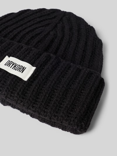 Produktfoto, Mütze aus Woll-Mix mit Alpaka-Anteil mit Label-Patch von DRYKORN, schwarze Strick-Optik, breiter Umschlag, Nahaufnahme.