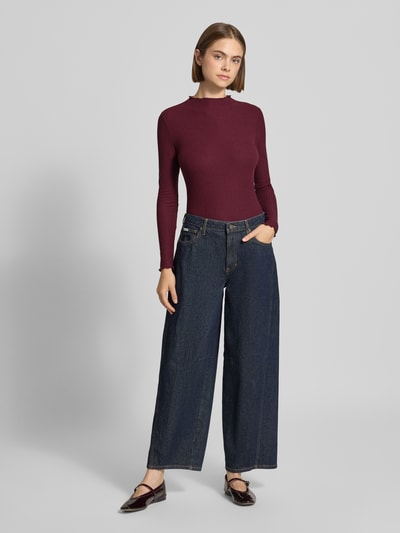 Frauenmodel trägt Slim Fit Langarmshirt mit Viskose-Anteil Modell 'EMMA' von ONLY in Dunkelrot zu weiter Jeans, Ganzkörperansicht von vorne, Damen Langarmshirt von ONLY.